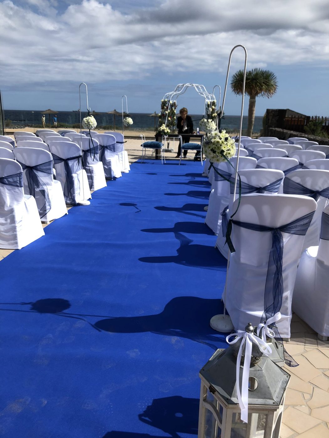 Alfombra azul y sillas blancas de ceremonia en la playa