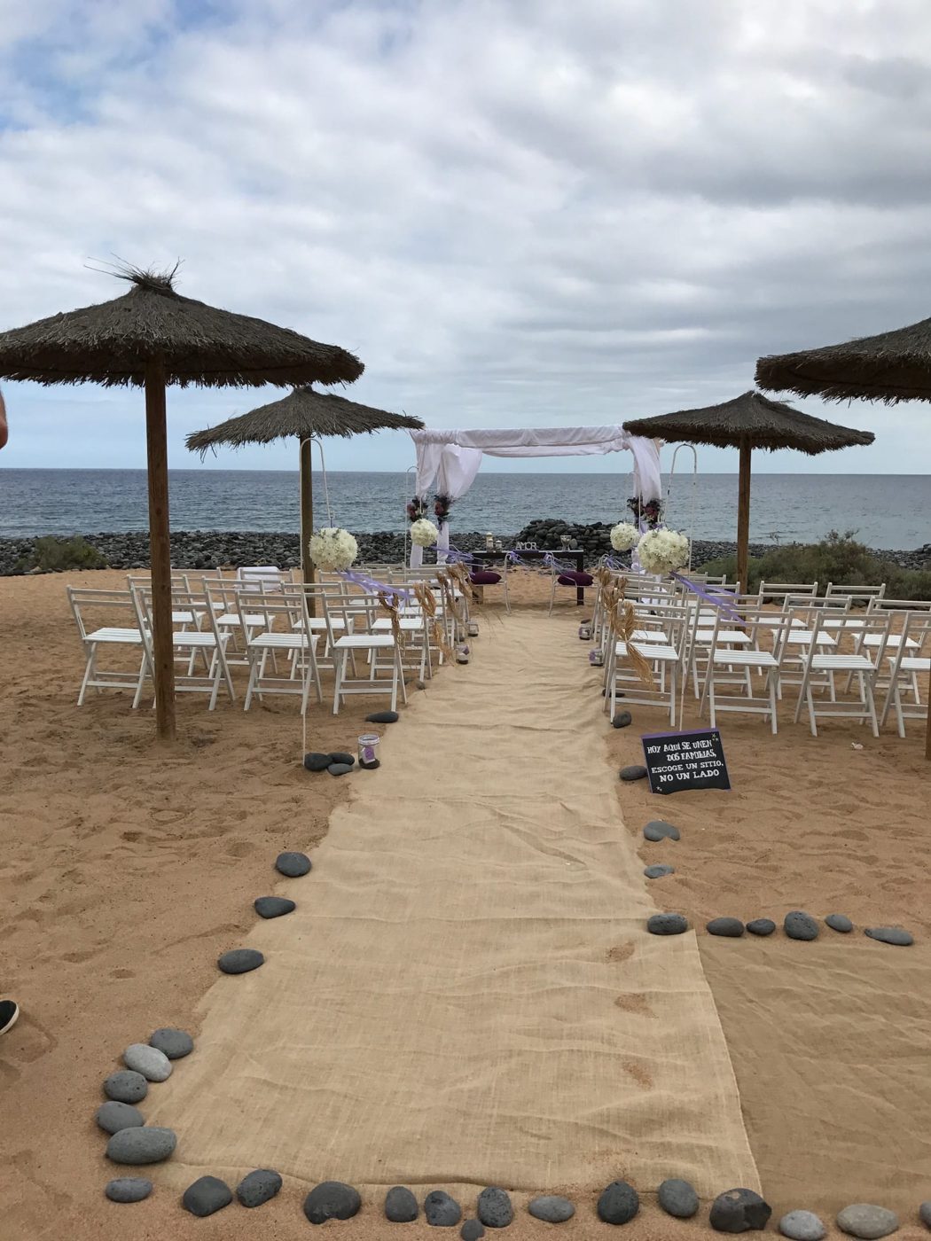 Arco blanco de ceremonia en la playa junto a sombrillas