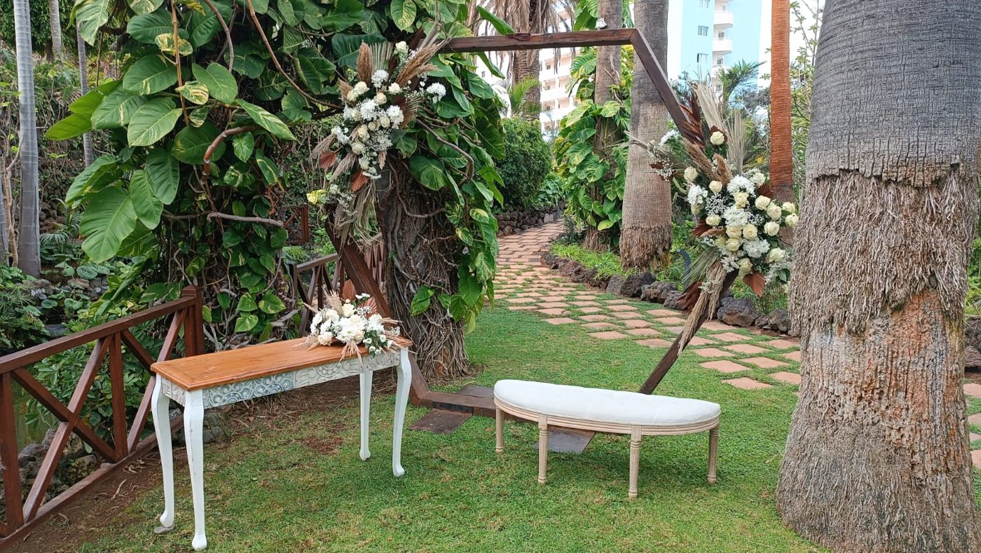 Arco de madera en jardín con banco y mesa consola decorados con flores