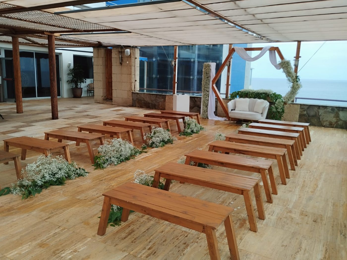 Mesas de madera en terraza junto al sofá y arco de ceremonia