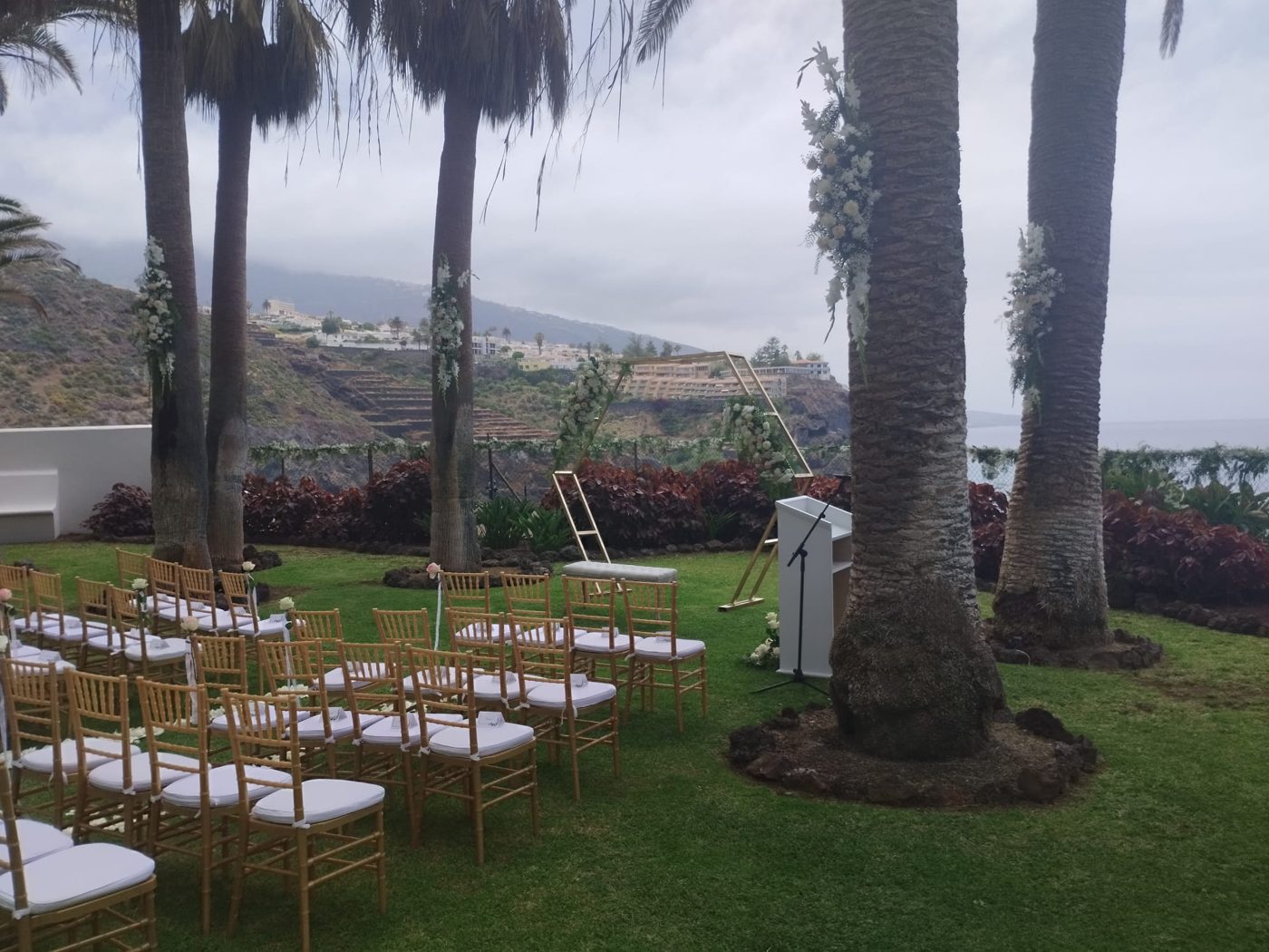 Sillas doradas y atril de ceremonia entre palmeras con vistas a la montaña